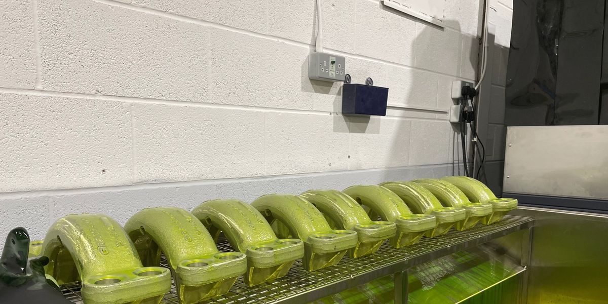 Machined components coated in green fluorescent penetrant, draining on a rack