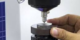 A hardness tester indenter lowered onto a prepared metal disc