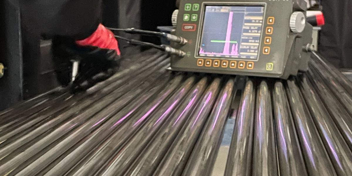 An ultrasonic flaw detector sitting on a bundle of tubes, with an A-scan on its screen